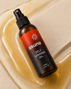 Asuno Self Tanning Oil bottle resting in golden oil — lightweight, fast-absorbing formula